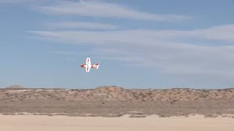 Small aircraft flying low over a desert landscape with hills in the background.