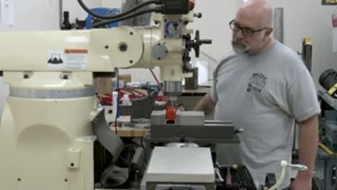 Man in a workshop standing near heavy machinery and milling equipment in an industrial setting.