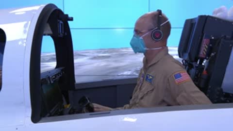 Pilot sitting in a flight simulator cockpit wearing a headset and face mask.