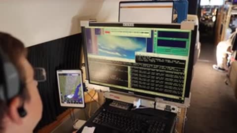 A person sits at a computer monitor inside an aircraft cabin.