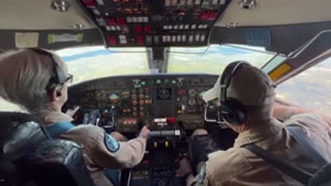 Two pilots sit in the cockpit of an aircraft in flight.