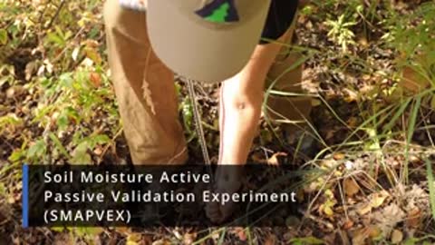 A person stands in a grassy field conducting soil moisture measurements.