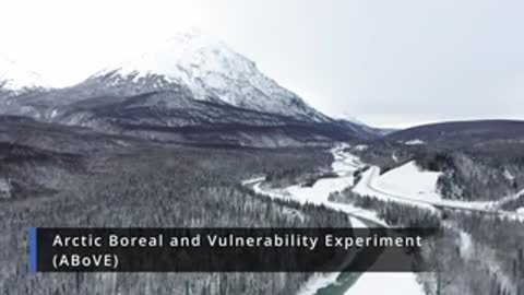 An aerial view shows a winding river through a snowy valley.