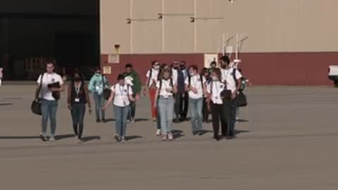 A group of people walks across a tarmac towards the camera.