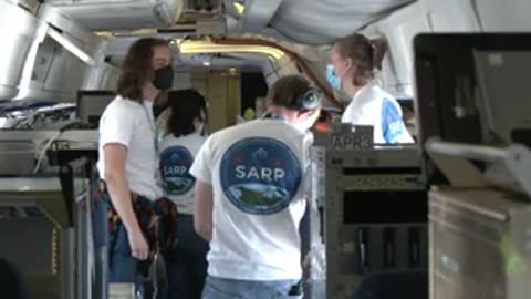 People stand inside an aircraft cabin wearing face masks and SARP shirts.