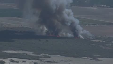 Smoke rises from a fire in a rural landscape viewed from above.