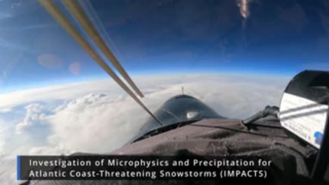 An aerial view looks forward from a high-altitude aircraft cockpit window.