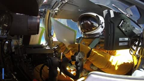 A pilot in a high-altitude pressure suit sits in a cockpit.