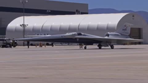 Wide shot of the X-59 aircraft parked near a large hangar.