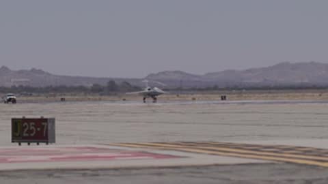Distant wide view of the X-59 aircraft moving down a runway.