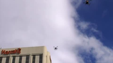 Drone flying near skyscraper with cloudy sky backdrop.