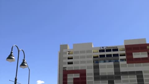 Drone flying near top of patterned building against blue sky.