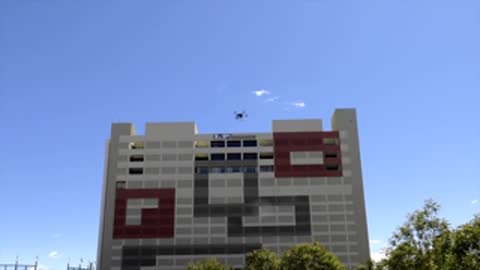 Drone flying past textured building exterior against blue sky.
