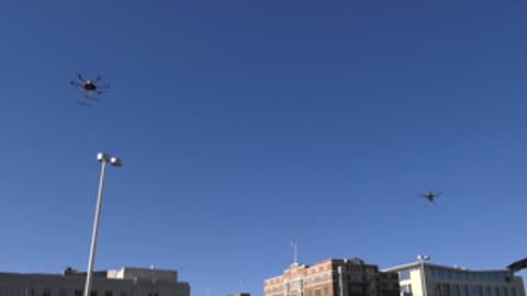 Multiple drones flying in formation against clear blue sky.