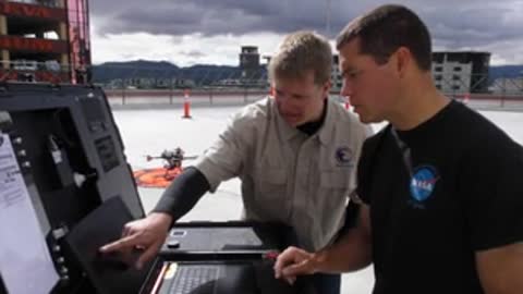 Two men operating equipment and looking at laptop outdoors.