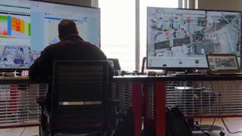 Man sitting at desk viewing multiple data screens in control room.
