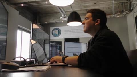 Man sitting at desk typing on laptop in office setting.
