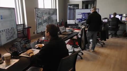 Control room with multiple desks, monitors, and working personnel.