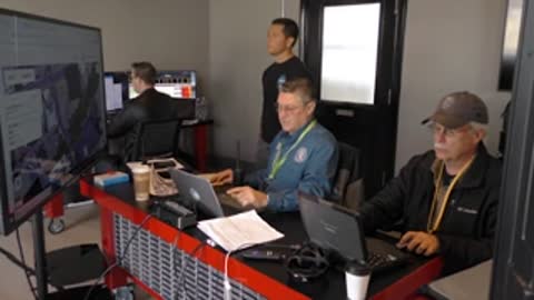 Multiple people working at desks with computers in office room.