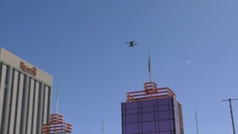 Drone flying in clear blue sky near city buildings.