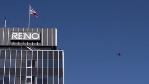 Drone flying past a skyscraper with Reno sign and flag.