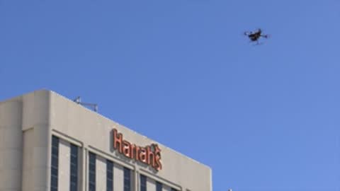 Drone flying in clear blue sky near building with Harrah's sign.