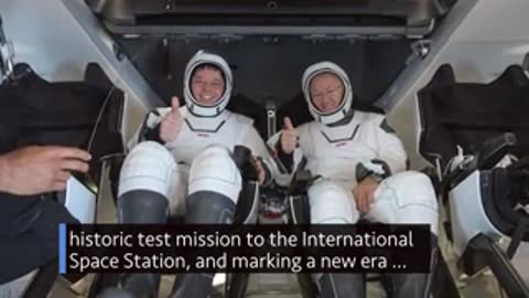 Two astronauts in space suits sitting inside a capsule.