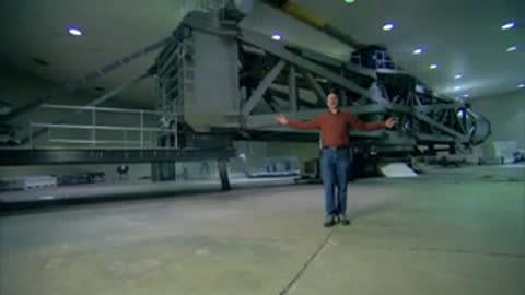 Man standing with arms outstretched in a large indoor testing facility