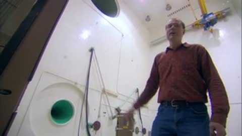Man speaking in a cleanroom, followed by workers in protective suits nearby