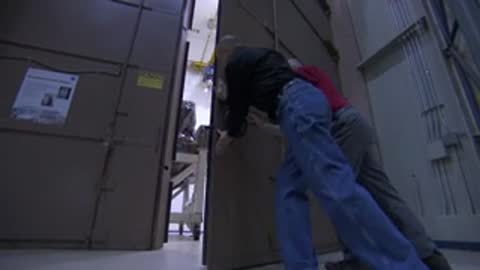 Engineers walking in a facility, two men closing a large door, and a red alarm light