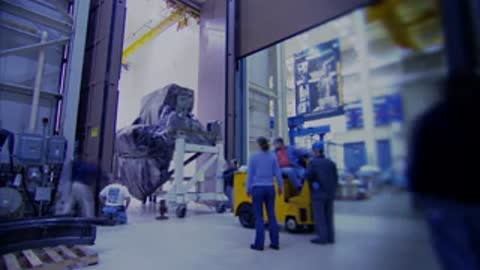 Workers and equipment moving inside a large industrial facility or hangar