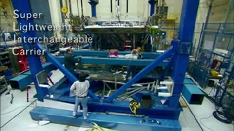 Workers operating a blue mechanical testing frame in an industrial hangar