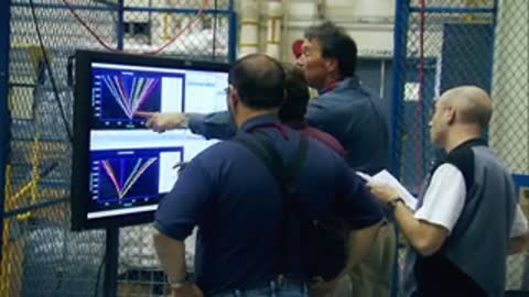 Engineers reviewing and discussing charts displayed on a large monitor