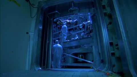 Technician in cleanroom suit preparing equipment near a vacuum chamber hatch