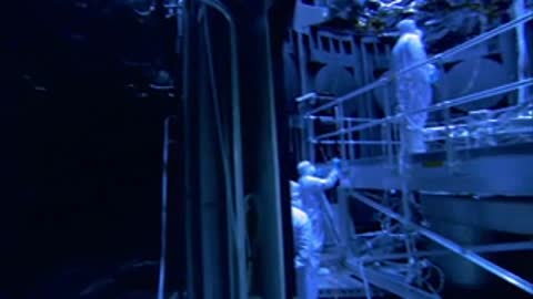 A medium shot of workers in white cleanroom suits servicing equipment inside the chamber.