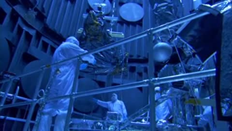 A medium shot of engineers in white protective suits working on hardware components.
