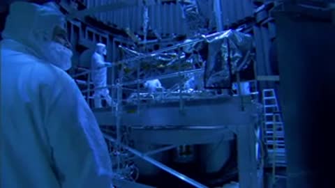 A close-up of a worker in a white cleanroom hood overlooking the testing area.