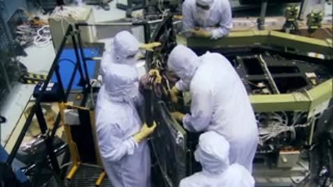 A high angle shot of workers in cleanroom suits assembling satellite components together.