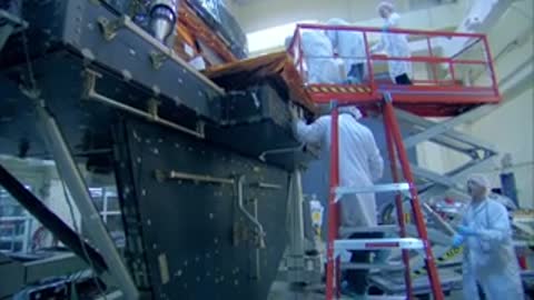A medium shot of technicians on a scaffold working on a large spacecraft structure.