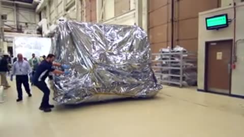 Workers pushing the large covered module across the floor on wheeled equipment