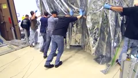 Group of technicians pushing the large wrapped module through a doorway area