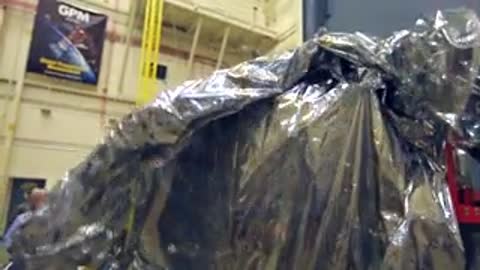 Man walking past the large covered payload module inside the spacious industrial hall
