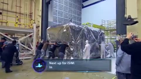 Team of workers pushing the covered module toward a large sliding facility door