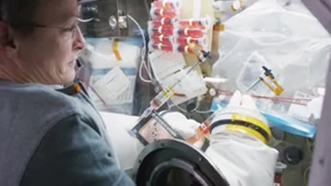 An astronaut handling a clear container in a glovebox