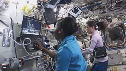 People work with computer equipment inside a space station module.