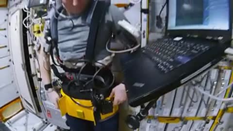 An astronaut adjusts equipment attached to a belt in microgravity.
