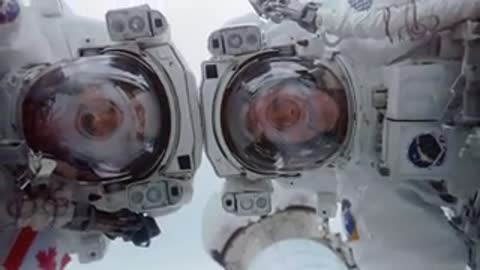 An astronaut works with equipment next to spacesuit helmets.