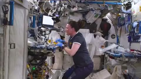An astronaut works at a workstation inside a space station module.