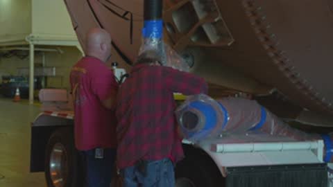 Close-up shot of two workers attending to equipment on a large rocket stage.