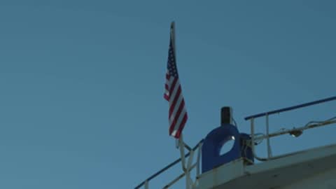 Static medium shot of an American flag waving on a boat against a blue sky.
